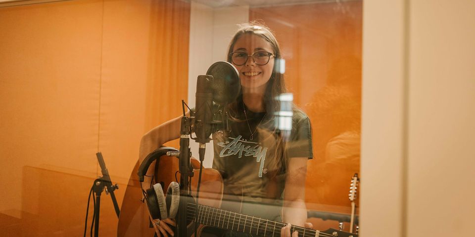 Female teenager playing guitar in recording booth