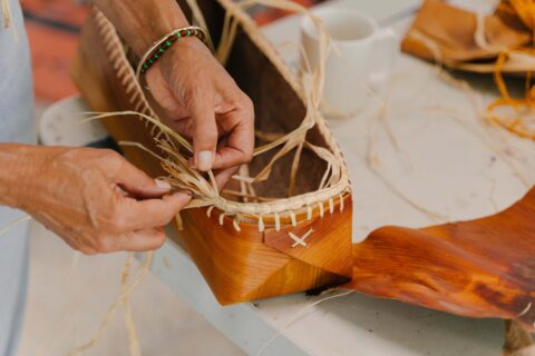 A close up image of two hands weaving a traditional basket.